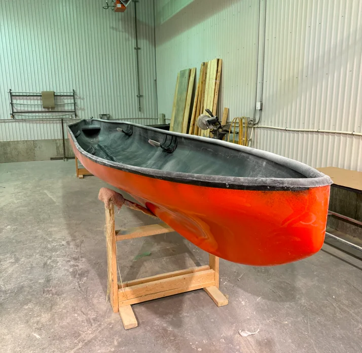 Réparation d'un canoë orange et noir sur des tréteaux dans l'atelier de HTM Composites